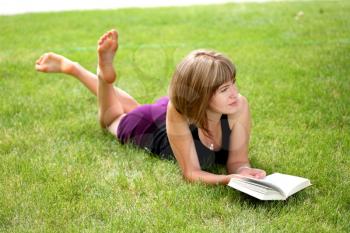 girl reading book outdoors laying on the green grass