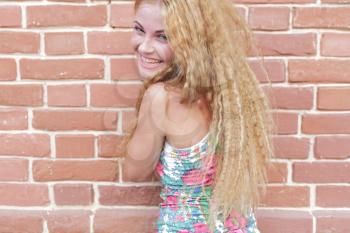 Beautiful woman with long blond hair standing against brick-wall and smiling