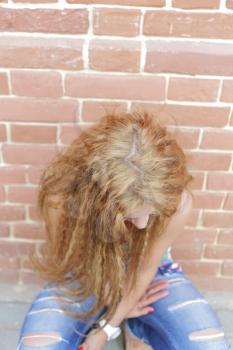 The girl with long hair sitting near wall looking to the ground