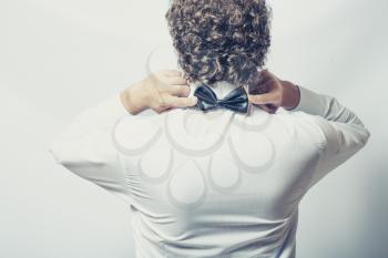 Bow tie on the back side. Strange or fun concept. Back view of an elegant young fashion man in tuxedo on gray background, toned image