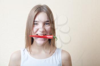 beautiful girl with red pepper in the teeth - organic food and health concept