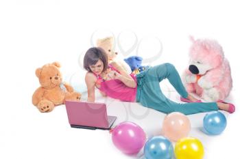 Young girl using a laptop near bear toys laying on white studio shot