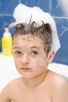Smiling little boy front view. Kid covered with soap bubbles against a blue wall in bathroom