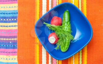 Radish, cucumber in blue bowl on red table cloth view from above