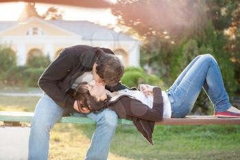 Happy couple against the background of park kissing sitting on the park bench, backlit composition, togetherness concept, love and tenderness