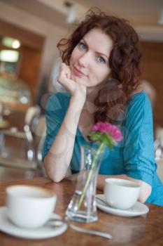 Redhead women sitting in the cafee with two cups of coffee and pink flower on the table befor and looking at camera and smiling