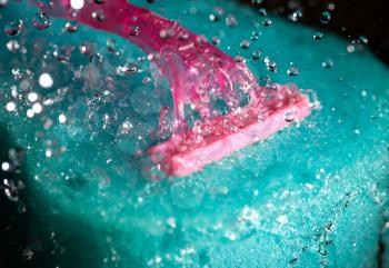 pink women shaving tool on the blue bath sponge, closeup with flying waterdrops