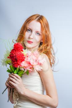 Cute 20s female with pretty flowers. Redhead women with bunch of flowers in studio on white. Blank expression.