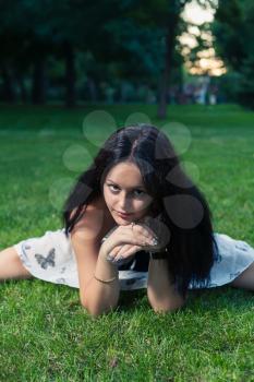Brunette lying on green grass and looking at camera