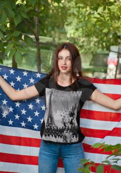 Beautiful patriotic young female student with the American flag held in her outstretched hands standing in the street..