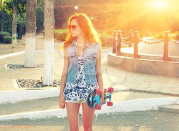 Pretty young woman backlit  standing with skateboard in her hands backlit by sunset