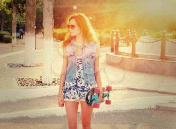 Young casual weared woman standing with skateboard in her hands.