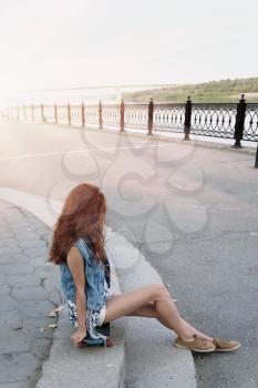 Red haired girl sitting near her scateboard vertical image
