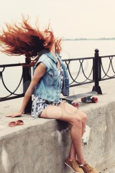 Toned image of young women sitting with skateboard on parapet and shaking her hair
