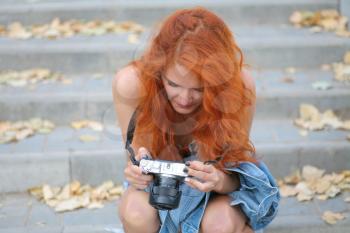 Young redhead woman photographer. Cute women halding modern camera in her hands and looking at screen inspect images