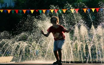  Boy in red shirt playing  wet near city park fountain. Happy summertime fun