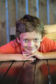 Smiling boy sitting in restaurant with his chin on hands