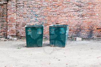 Two green dustbins outside against red brick wall in ghetto