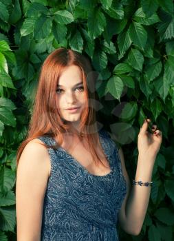 Young pretty red haired women standing against ivy wall and looking at camera with her hand rised