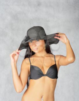  In black hat. Young black haired women posing in studio on gray