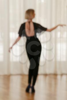 Defocused image Rear view of young woman with exellent body dancing in front of window curtain, toned color