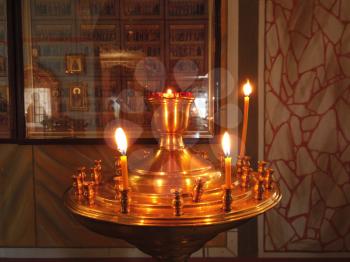 Astrakhan Russia - 10 October 2020: Candles burning on golden stand in front of the saints pictures on the wall. Orthodox church inside with burning candles on golden stand