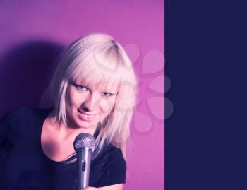 Lifestyle of young people concept: Blond model girl singer with a mic on pink background with copy space.