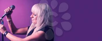 Blond haired woman set up the mic on mic-stand on pink violet background with a lot of copyspace. Banner for web site.