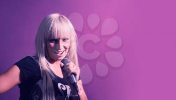 Blond woman sing with mic in karaoke on pink background with a lot of copyspace.