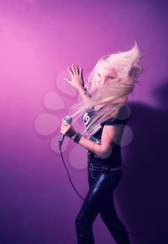Rock singer with mic. Karaoke lady with her blond hair in motion on pink background.