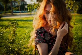 Amazing redhead lady wind swept hair covering her face with closed eyes, backlit by summer sun. Summertime mood.