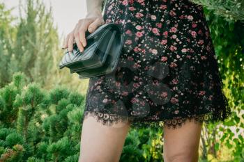 Stylish lady in summer dress walking alone in park with black leaser handbag.