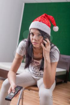 brunette women weared Santa hat with remote control in hands, calling by cell phone