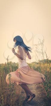 Jollyful lady in romantic wear dance in the fields with her black hair flying in an air, blurred motion shot.