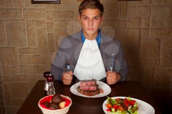 man holding a knife and a fork ready to eat a beef steak