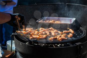 A professional cook prepares shrimps on the grill outdoor, food or catering concept