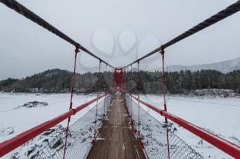 Suspension hanging bridge above winter frozen mountain Katun river, Altai mountains, Siberia, Russia