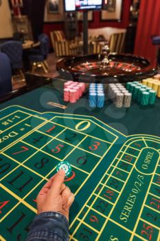 Casino, gambling and entertainment concept - male hand with stack of poker chips on a green table background