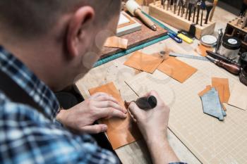 Man working with leather textile at a workshop. Concept of handmade craft production of leather goods.