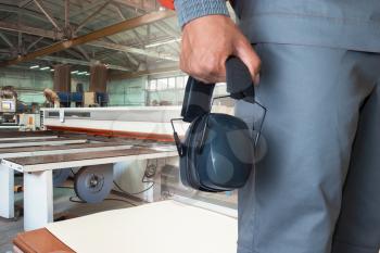 Wooden furniture production. Worker wearing protective headphones at factory