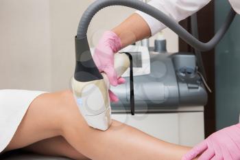 Closeup photo of woman getting laser hair removal procedure on her legs in modern clinic. Cosmetology and SPA concept