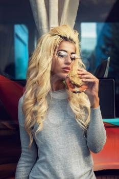 Fast street food concept - beauty young blonde woman eating a burger and soda water near the food truck