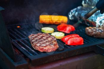 Beef steaks with vegetables on the grill with flames