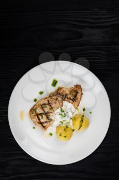 Grilled pork meat with mushroom sauce and potato on white plate on wooden black background