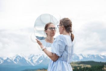 Woman standing in in summer Altai mountains in Kurai steppe and holding circle mirror. Creative travel concept