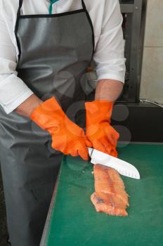 Chef cutting salmon fish on fillet with knife