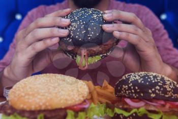 Man eating burgers at table, closeup photo