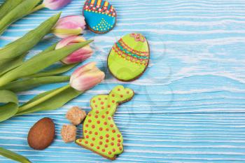 Composition of tulips and gingerbread cookies on white and blue wooden background for Happy Easter.