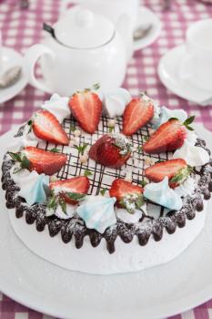 Tasty strawberry cream cake on checkered table, with tea set
