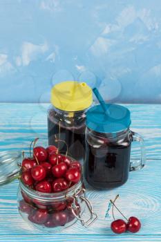 Cherry juice with glass jar of berries on blue wooden background